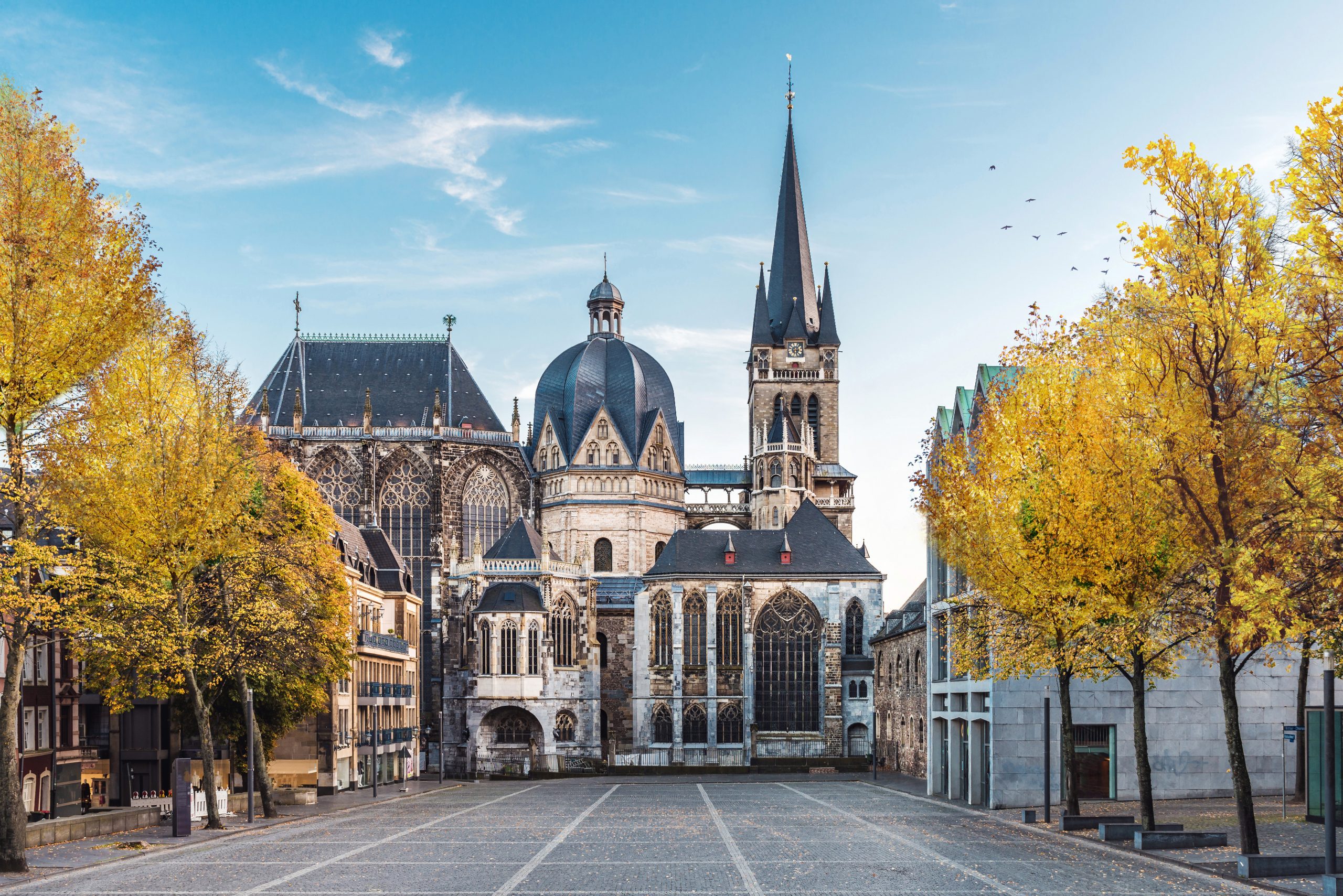 German cathedral in Aachen during fall with yellow leafs at trees with blue sky